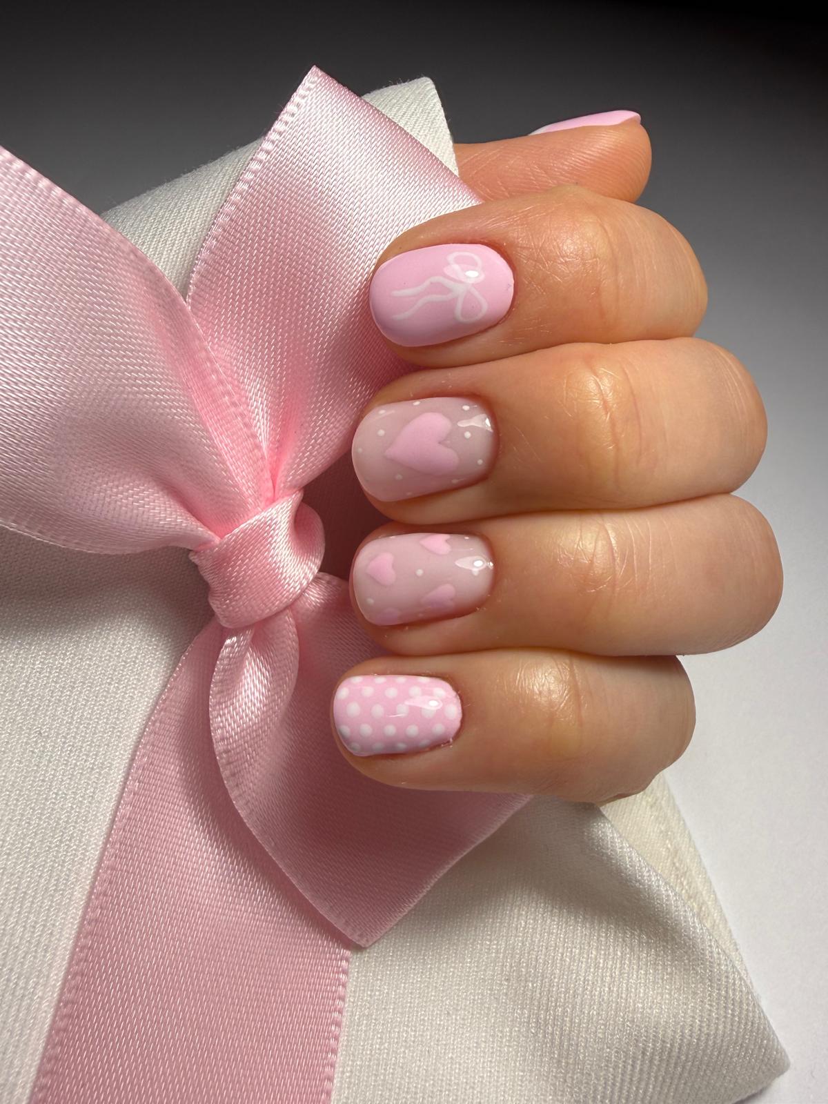 Jasnoróżowe paznokcie z teksturą w kropki, dłoń trzyma różową kokardę